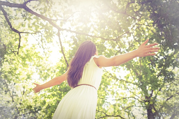A woman with open arms looking up at trees in a forest. Goddess Artemis Connection with Nature - Carla Lima Online Course
